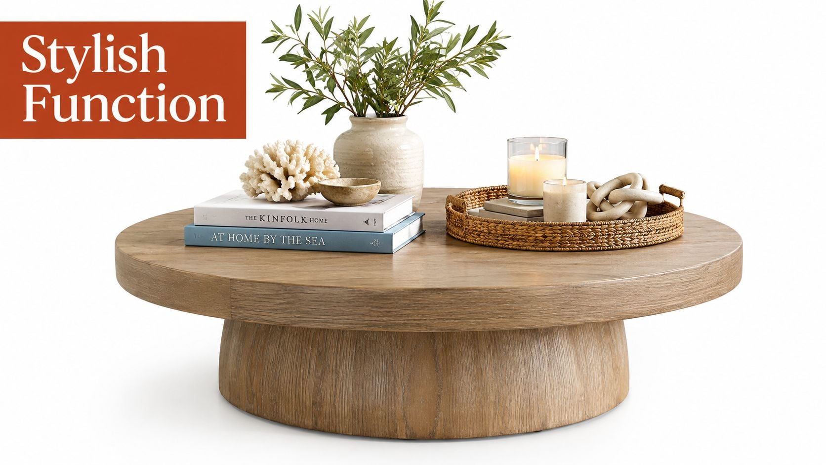 A large wooden round coffee table decorated with books, a vase, coral, candles, and a woven tray.